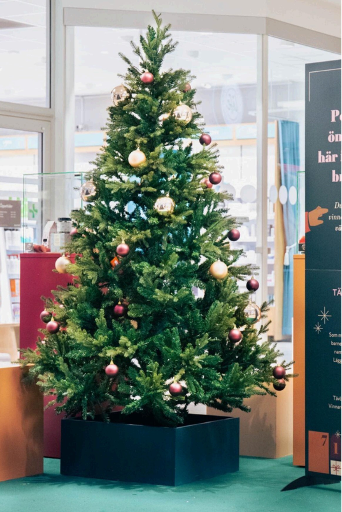 Julgran med rosa och guldfärgade kulor i en svart julgransfot byggd för butik