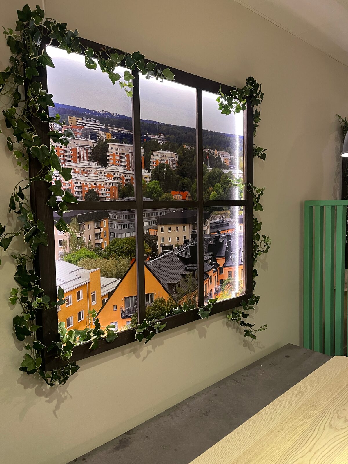 Belyst fönsterinstallation med stadsmotiv och dekorativ murgröna