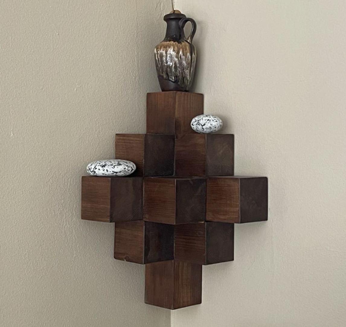 Skulpturalt vägghängt objekt i mörkt trä placerat i ett hörn