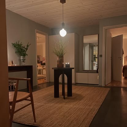 Mörkt sidobord i trä med valvformade ben i en hall med varm pendelbelysning