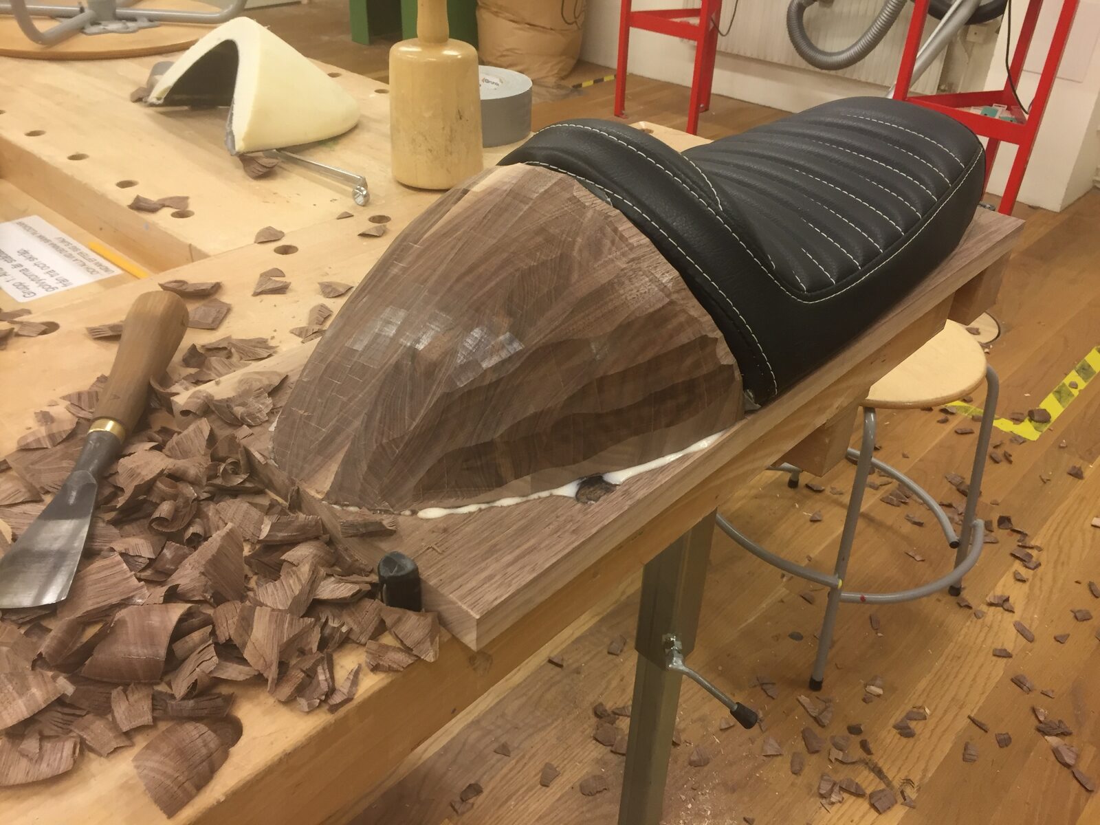 Motorcykelsadel under formgivning i verkstaden, handhuggen bakdel i valnöt