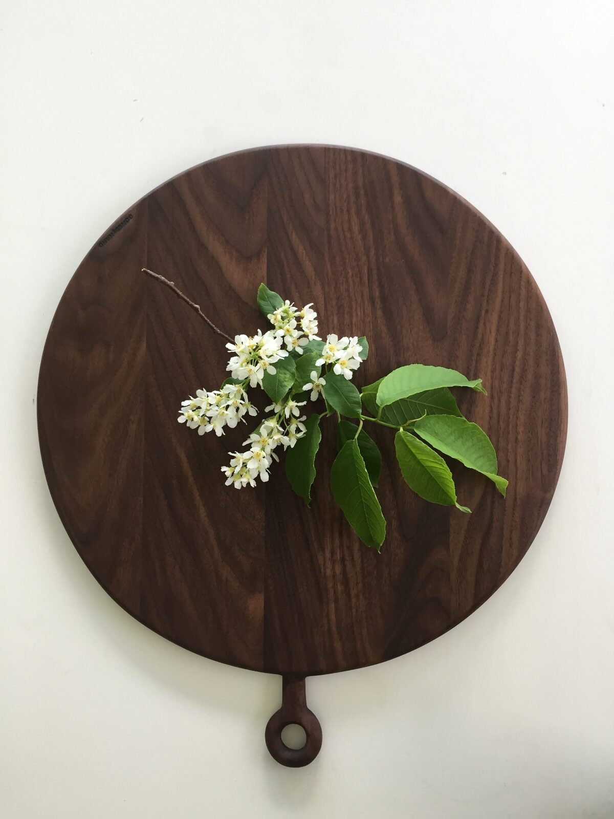 Rund serveringsbricka i valnöt med blommande kvist ovanpå